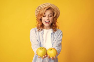 Elma tutan genç bir kadın mutlu ve havalı bir gülümsemeyle gülümsüyor, dişlerini gösteriyor. Sarı arka planda, elinde elma tutan mutlu ve güzel bir kadın görüntüsü.