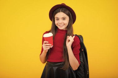 Kahve fincanı olan genç bir çocuk sarı stüdyo arka planında izole edilmiş. İçki içen kız içeceğini aldı. Mutlu ergen portresi. Gülümseyen kız