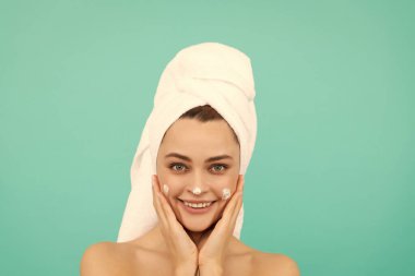 Neşeli genç bayan mavi arka plana yüz kremi sürüyor..