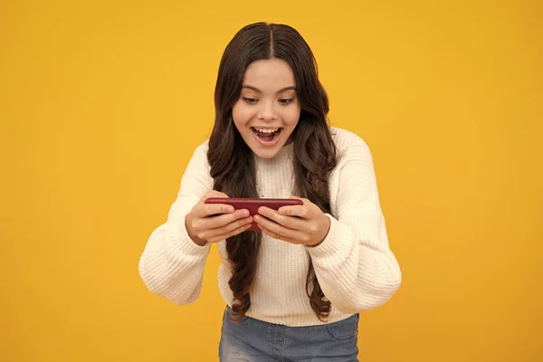 Excited teenager girl 12, 13, 14 years old with smart phone. Hipster teen girl types message on cellphone, enjoys mobile app. Kid hold smartphone texting in online social media. Internet addiction