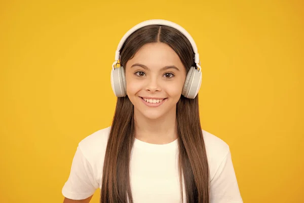 Teenager child girl in headphones listening music, wearing stylish casual outfit isolated over yellow background. Happy teenager portrait. Smiling girl
