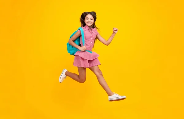 School girl in school uniform with school bag. Crazy run and jump. Schoolchild teenager hold backpack on yellow isolated background