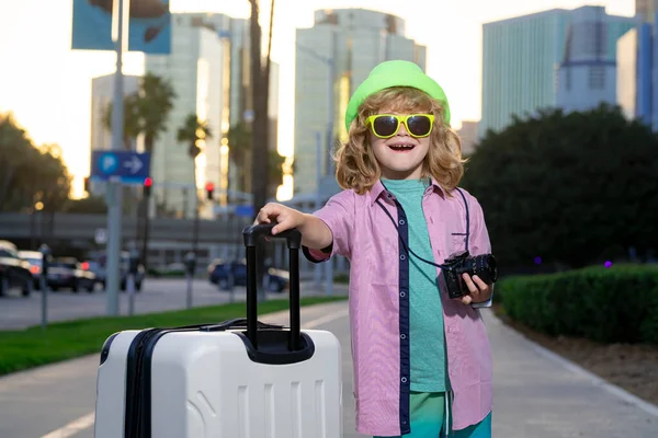 Kids travel. Happy child boy carrying travel suitcases outdoor on city street. Travel lifestyle and dreams of travel
