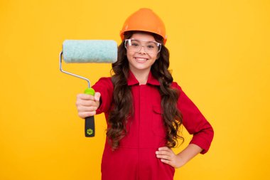 Miğferli çocuk müteahhidi. Fırça aletli ya da boya silindirli genç kız ressam. Sarı arka planda izole edilmiş tamir işindeki çocuk. Çocuk yenileme konsepti. Mutlu genç kız