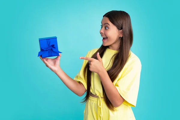 Excited face, cheerful emotions of teenager girl. Teenager child holding gift box on blue isolated background. Gift for kids birthday. Christmas or New Year present box