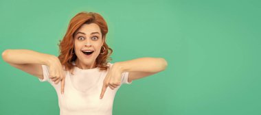 Woman isolated face portrait, banner with copy space. amazed redhead woman pointing finger down on blue background, copy space, shopping sales