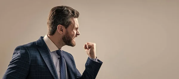Aggressive man businessman in suit make threaten gesture shaking fist at somebody, threatening. Man face portrait, banner with copy space. Business man in suit, isolated studio background