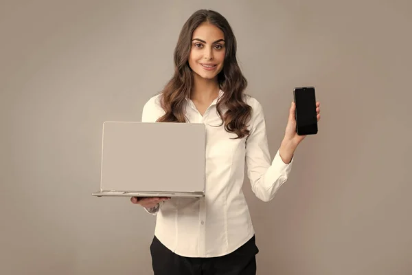Happy girl using mobile phone and laptop. Woman showing empty laptop screen, mock up template with copy space