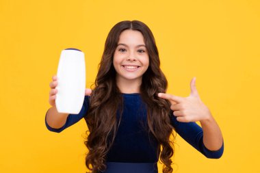 Şampuan kremi kullanan bir çocuk. Günlük kozmetik bakım. Gençlerin elinde saç ve cilt bakımı şişesi var. Güzellik sağlığı ve kozmetik ürünleri. Mutlu yüz, pozitif ve gülümseyen genç kız duyguları