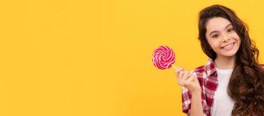 Uzun kıvırcık saçlı komik çocuk sarı arka planda lolipop karamel şekeri tutuyor barış jesti gösteriyor, çocukluk.
