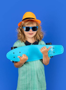 Çocuk mavi arka planda uzun tahta tutuyor. Pennyboard 'u olan çocuk. Bozuk paralı neşeli küçük çocuğun stüdyo fotoğrafı.