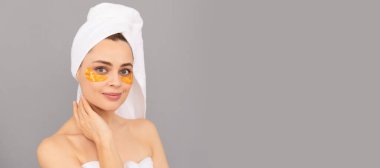 Göz bantları, göz altı bantları. Terry havlusu olan genç bir kadın cilt için altın göz bandı kullanır. Güzel kadın, izole edilmiş yüz portresi, taklit alanı olan pankart.