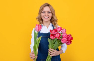 Sarı arka planda bahar lale çiçekleri olan önlüklü gülümseyen genç kadın..