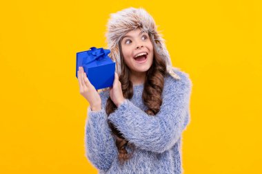 Sarı arka planda hediye kutusu olan şapkalı, uzun saçlı hayret bir çocuk..