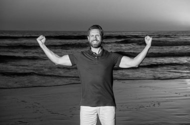 Sahilde başarılı bir adam. Gündoğumu plajındaki beyaz adam. Gömlekli sakallı adam. Yaz modası. Yaz tatili. pozitif duygular. Gün batımında deniz üzerinde sakallı mutlu adam başarısını kutluyor..