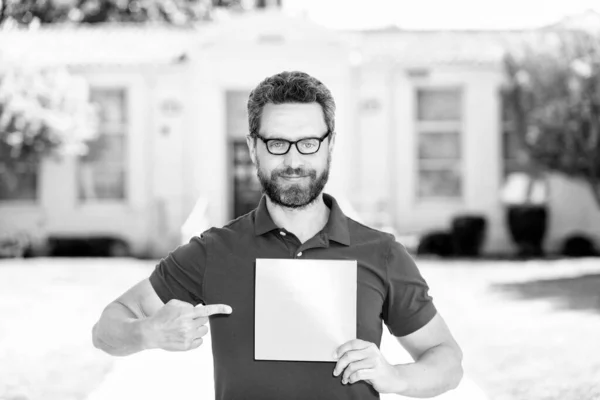 smiling man nerd pointing finger on paper sheet presenting advertisement, copy space, promotion.