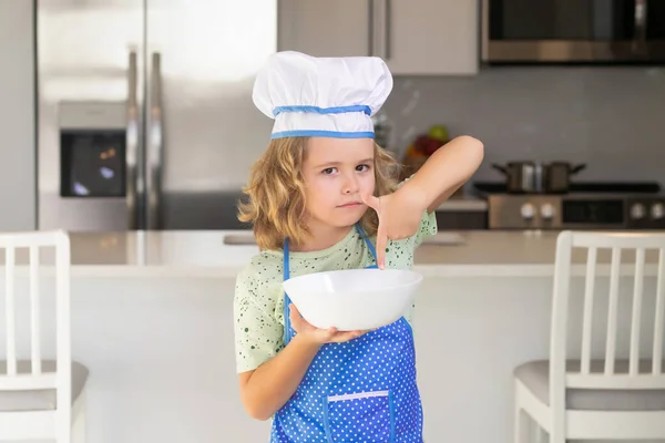 Child chef cook with cooking plate. Child in chef hat and apron preparing food in the kitchen. Cooking children. Child boy with apron and chef hat preparing a healthy meal in the kitchen