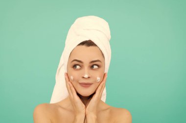 Neşeli genç bayan mavi arka plana yüz kremi sür..