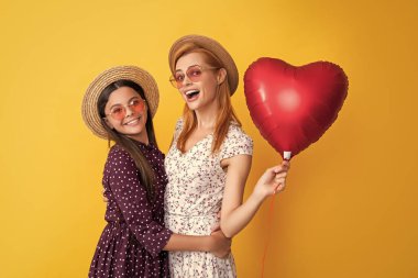 Anne ve kızı gülümsüyor. Sarı arka planda aşk balonu var..