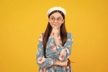 Düşünceli genç kız çenesine dokunur ve düşünür, düşünceli çocuk fikir üretir, sarı stüdyo arka planında izole bir şekilde poz verir. Düşünen zeki genç kız