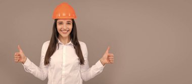 Koruyucu miğferli ve beyaz gömlekli mutlu kadın baş parmağını kaldırıyor, iyi sonuç. İzole edilmiş yüz portresi, taklit alanı olan pankart