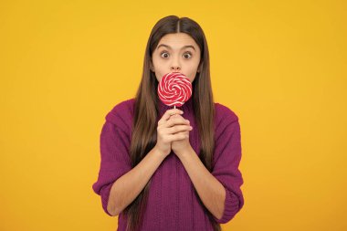 Teenage girl with candy lollipop, happy child 12, 13, 14 years old eating big sugar lollipop, sweets candy. Surprised emotions of young teenager girl