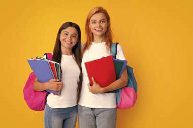 Okul, öğrenme ve eğitim konsepti. Okul çantalı ve kitapları öğrenmeye hazır anne-kız okul kızları. Okula dönelim. Anne ve çocuk izole edilmiş sarı stüdyo geçmişinde