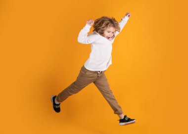 Heyecanlı çocukların zıplaması. Tüm vücudu küçük çocuk atlama tişörtü ve sarı arka planda izole edilmiş kot pantolon.