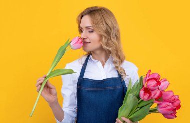 Sarı arka planda bahar lale çiçekleriyle önlükle gülümseyen genç bir kadın..