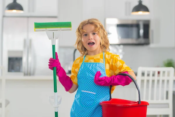 Child cleans at home concept. Kid cleaning with mop to help with housework. Little cute boy sweeping and cleaning, on kitchen background