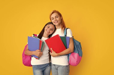 Okul, öğrenme ve eğitim konsepti. Okul çantalı ve kitapları öğrenmeye hazır anne-kız okul kızları. Okula dönelim. Anne ve çocuk izole edilmiş sarı stüdyo geçmişinde