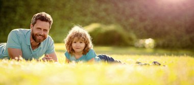 Açık yaz parkında baba ve oğulun bayrağı. Aile değeri. Çocukluk ve ebeveynlik. Ebeveyn rahat olsun. Küçük çocuk çimlerin üzerinde.