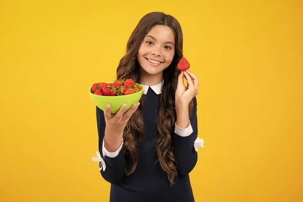 Child eating a strawberries. Happy smiling teen child hold strawberry bowl on yellow background. Healthy natural organic vitamin food for kids, strawberry season