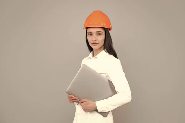 Young woman in hard hat helmet with laptop computer isolated on grey background. Architect woman wear helmet and shirt. Business woman, construction manager, builder