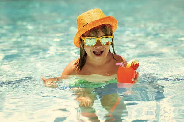 Child drink cocktail in swimming pool. Active healthy lifestyle, swim water sport activity on summer vacation with child. Fashion summer kid boy in hat and sunglasses