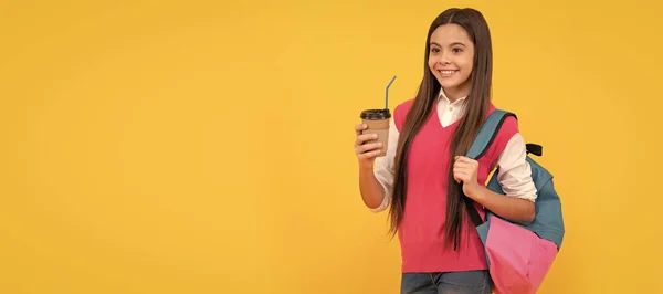 happy teen school girl with backpack drink takeaway cocoa on yellow background, lunch. Banner of school girl student. Schoolgirl pupil portrait with copy space