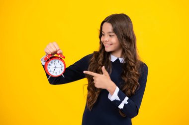 Portrait of teenage girl with clock alrm, time and deadline. Studio shot isolated on yellow background