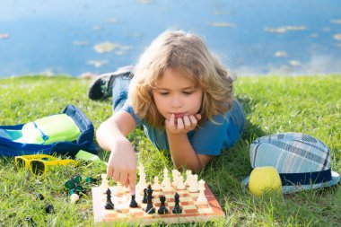 Küçük çocuk parkta satranç oynuyor. Çocuk dışarıda masa oyunu oynuyor. Düşünen çocuk beyin fırtınası ve satranç fikri