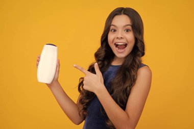 Teenager child girl with bottle shampoo conditioners or shower gel. Kids hair care. Hair cosmetic product, shampoo bottle. Happy girl face, positive and smiling emotions