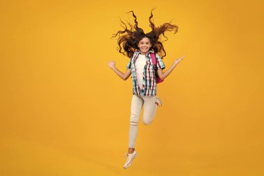 Okul üniformalı, sırt çantalı bir kız. Sarı izole edilmiş genç kız öğrenci. Okul boş vakitlerinde. Çılgınca koş ve atla. Öğrenim ve eğitim çocukları