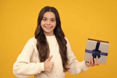 Happy face, positive and smiling emotions of teenager girl. Teenager child holding gift box on yellow isolated background. Gift for kids birthday. Christmas or New Year present box