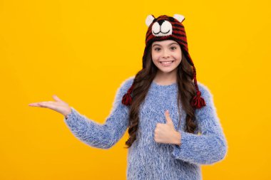 Sarı arka planda, kışlık şapkalı ergen bir kız. Kış Noel tatili, yeni yıl havası. Çocuklar sıcak kıyafetler giyer. Mutlu ergen, pozitif ve gülümseyen genç kız duyguları