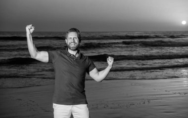 Başarıyı kutlamak. kopyalama alanı. Gün batımında deniz üzerinde sakallı mutlu bir adam. Sahilde başarılı bir adam. Sunrise Beach 'teki adam. Gömlekli sakallı adam. Yaz modası. Yaz tatili. pozitif duygular.