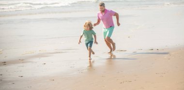 Babalar ya da aile günü. Baba ve çocuk yaz günü. Baba ve çocuk dışarıda eğleniyorlar. Çocukluk ve ebeveynlik. Baba oğul sahilde koşuyor. Aile seyahati ve tatil.