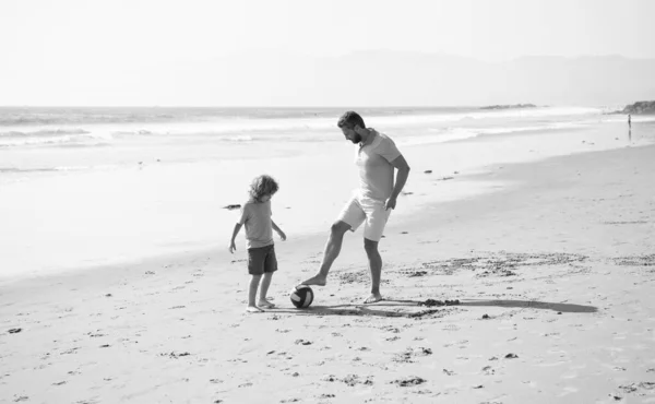 happy father and son playing football having fun on summer sandy beach family vacation, childhood.