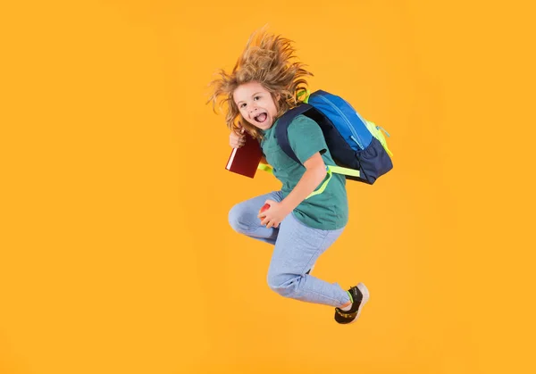 Full length of excited kid jumping. Back to school. Full length body of little school kid jumping having fun isolated yellow color background. Crazy school boy jump