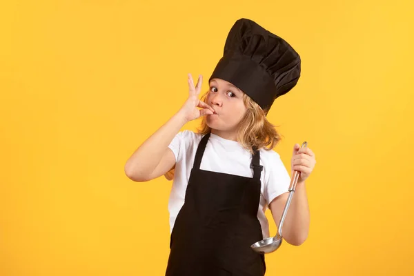 Funny kid chef cook with kitchen ladle, studio portrait. Kid in cooker uniform and chef hat preparing food on studio color background. Cooking, culinary and kids food concept