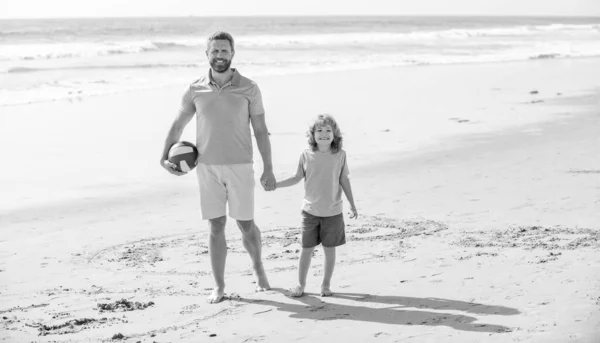 daddy with kid boy on summer day. weekend family day. dad and child having fun outdoors. childhood and parenting. family holidays. sport activity. happy father and son walk with ball on beach.