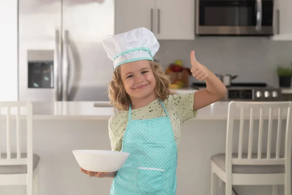 Child chef cook with cooking plate. Child chef cook is learning how to make a cake in the home kitchen. Child making tasty delicious. little boy in chef hat and an apron cooking in the kitchen