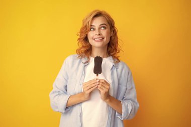 Young woman eat ice creams with chocolate glaze on yellow background. Funny redhead woman with ice cream